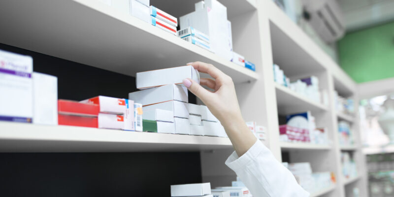 Closeup view of pharmacist hand taking medicine box from the shelf in drug store.