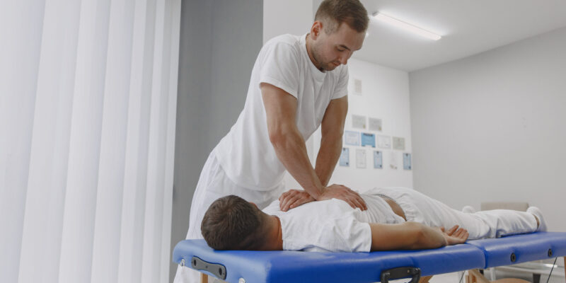 Man in the medical office. Physiotherapist is rehabilitating back.