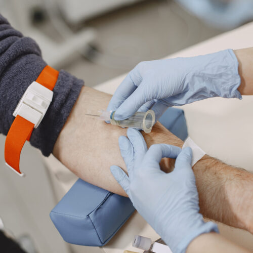 Skillful nurse is doing blood test for man in clinic. Man in a medical mask.