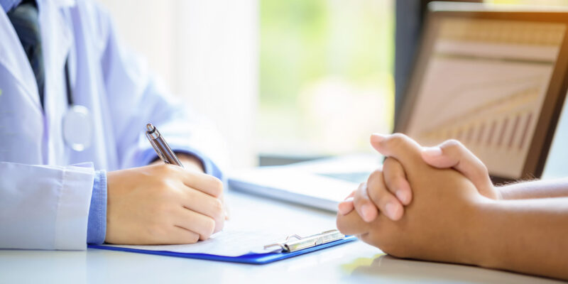 Doctor man consulting patient while filling up an application form at the desk in hospital. Medicine and health care concept