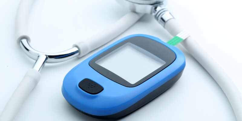 Blood glucose meter and stethoscope on white background